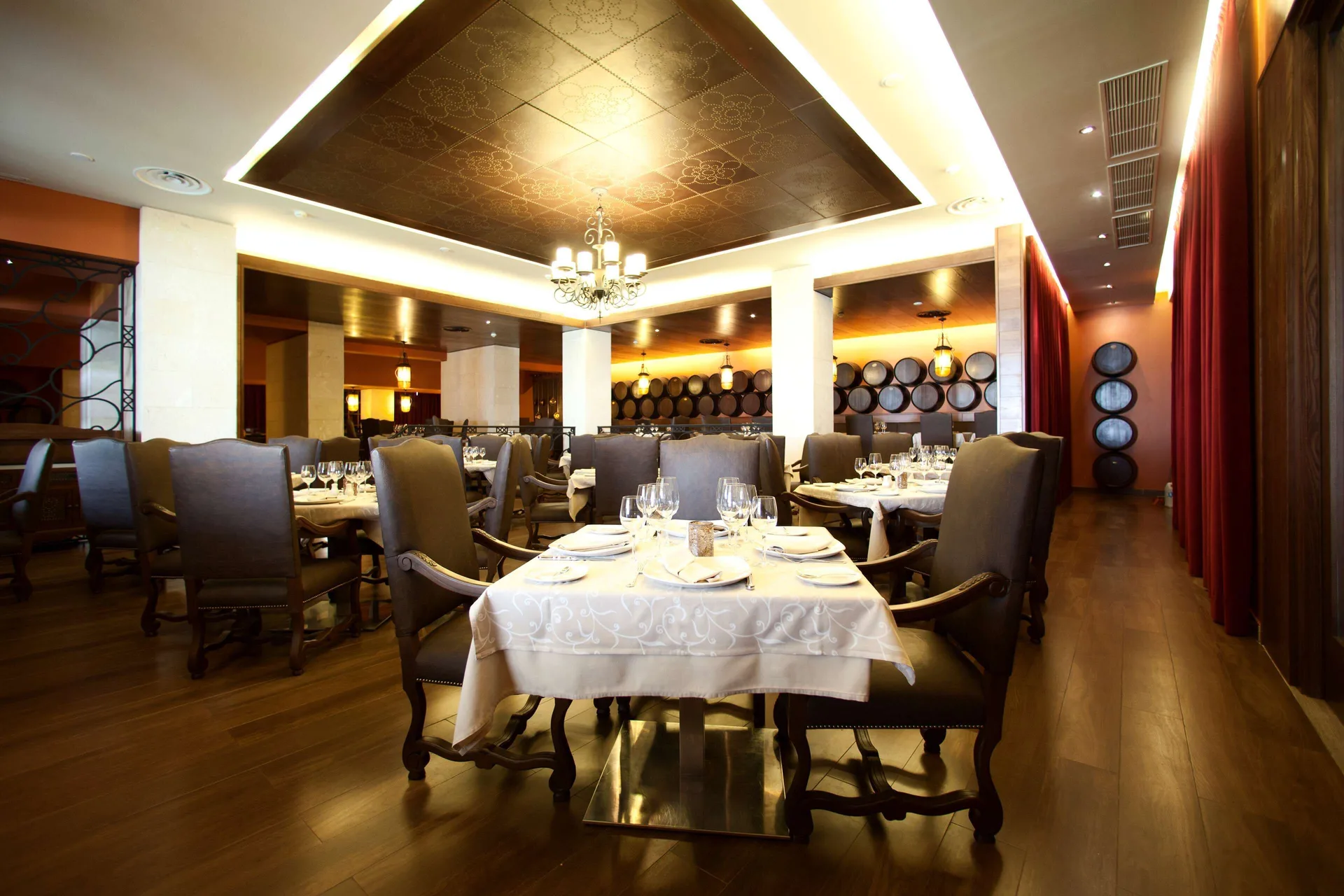Formal dining room with round tables, wine barrels, and chandelier at Barceló Bávaro Palace.