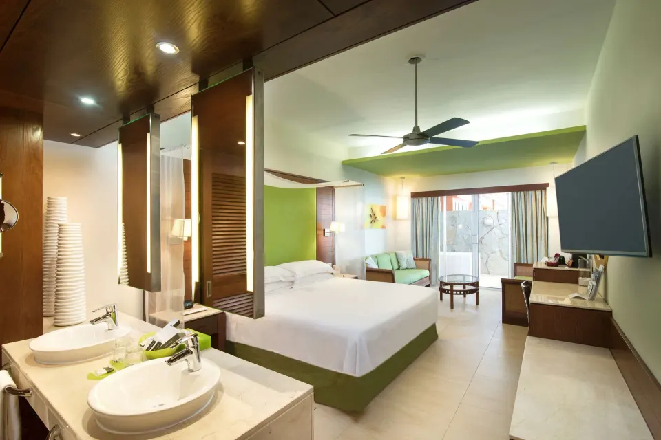 Junior Suite with king bed, open vanity area, sofa, balcony doors, and wall TV at Barceló Bávaro Palace.
