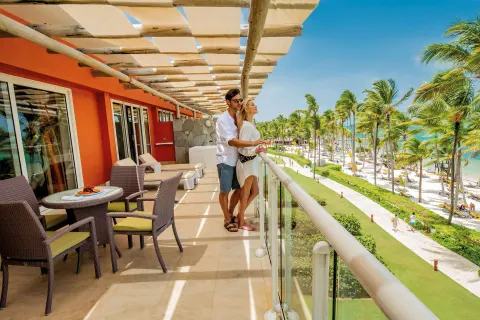 Sea View Suite balcony at Barceló Bávaro Palace with seating, guests, palm trees, beach, and ocean.