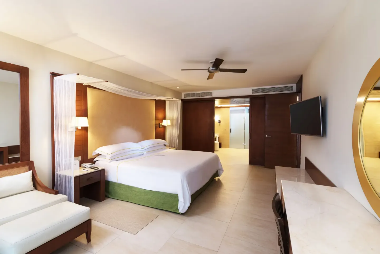Sea View Suite bedroom at Barceló Bávaro Palace with king bed, chaise lounge, desk, TV, and bathroom entry.