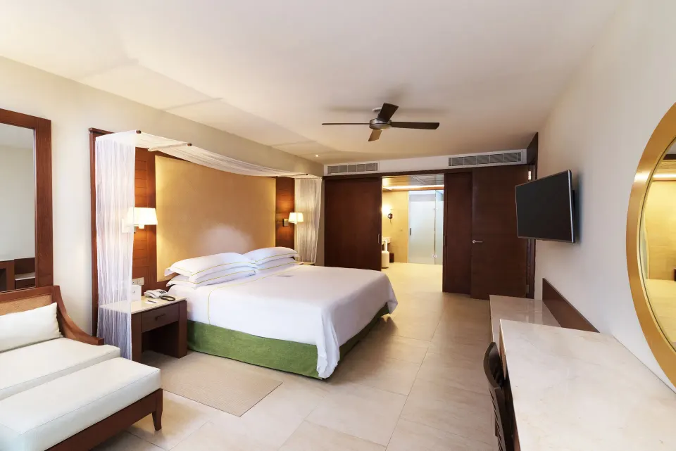 Sea View Suite bedroom at Barceló Bávaro Palace with king bed, chaise lounge, desk, TV, and bathroom entry.