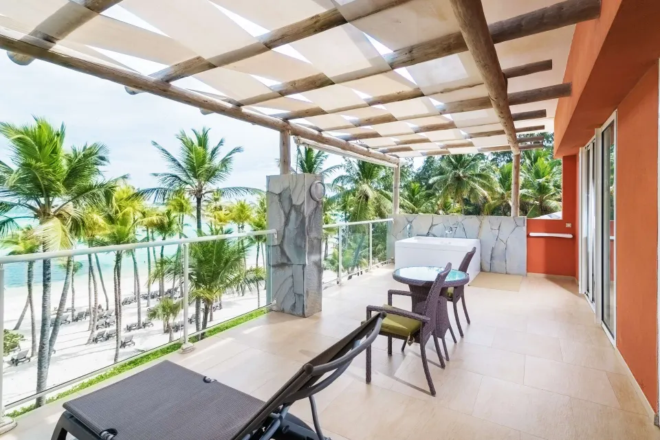 Sea View Suite terrace at Barceló Bávaro Palace with lounge chair, dining set, and ocean beyond palms.
