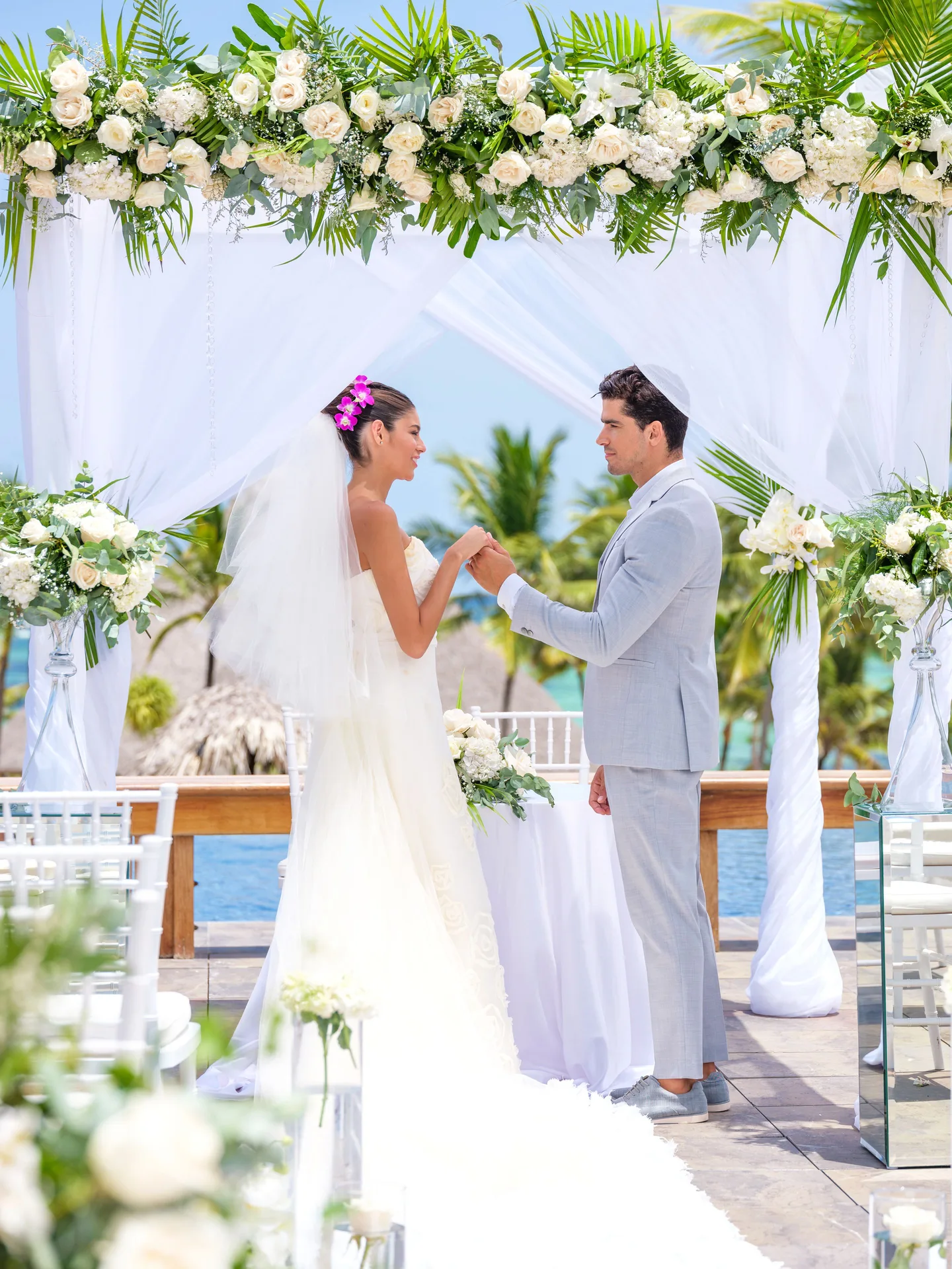 Bride and groom under a white floral wedding arch at Barceló Bávaro Palace.