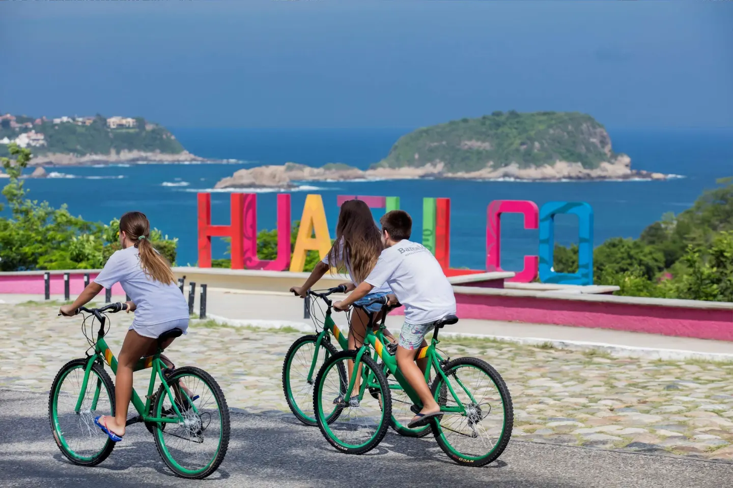 Cyclists pass a colorful Huatulco sign overlooking the bay near Barceló Huatulco.