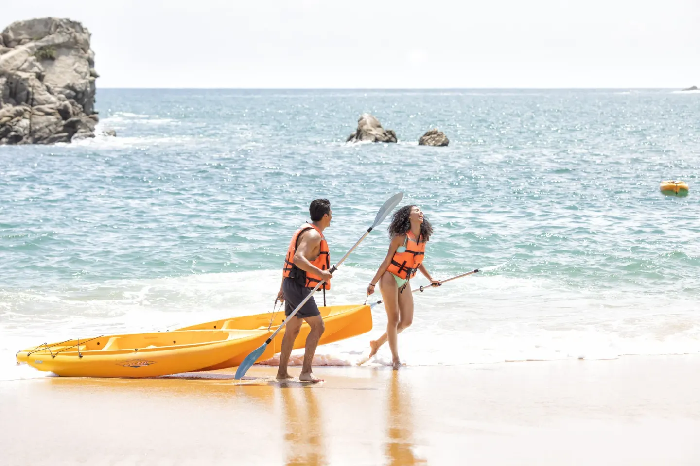 Two kayakers pull a yellow kayak onto the beach at Barceló Huatulco.
