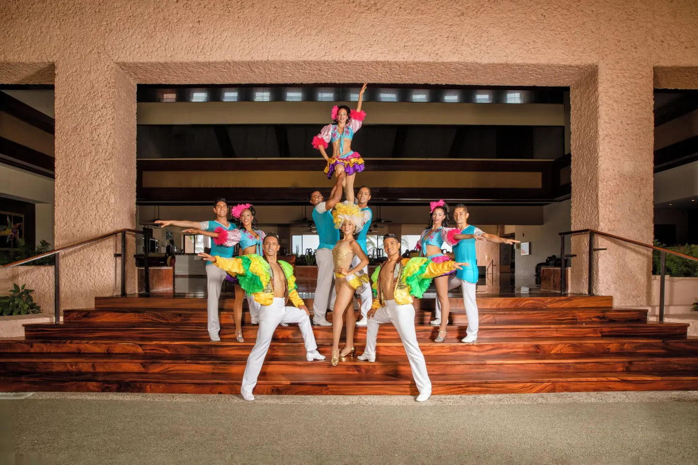Dancers in colorful costumes pose on wooden lobby steps at Barceló Huatulco.