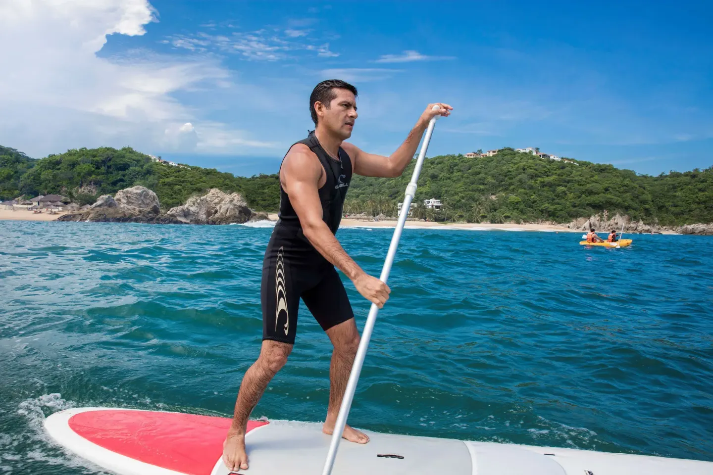 A man paddleboards on blue water near the beach at Barceló Huatulco.