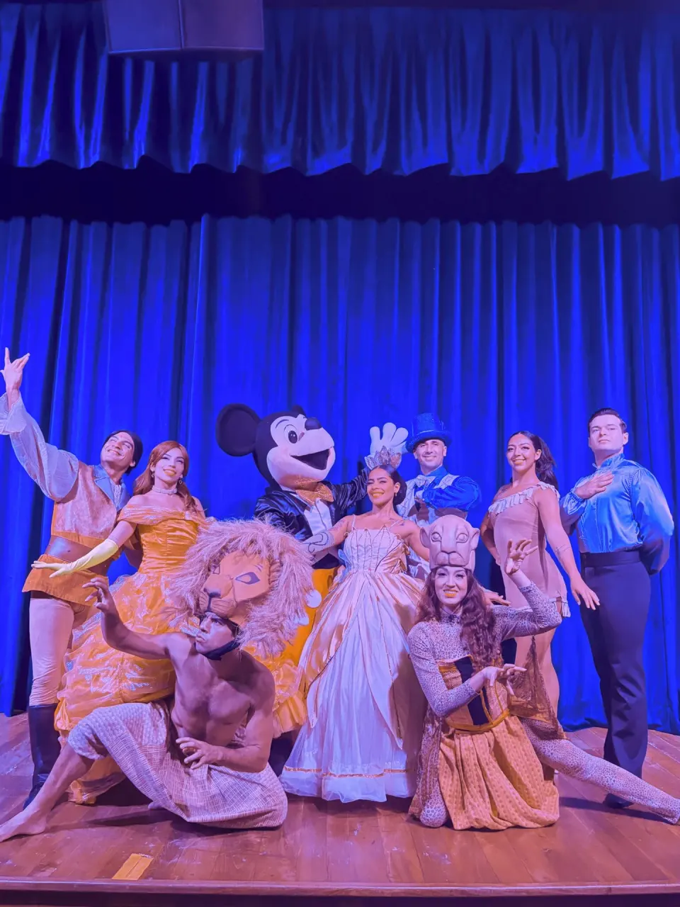 Stage cast in storybook costumes poses before blue curtains at Barceló Huatulco.