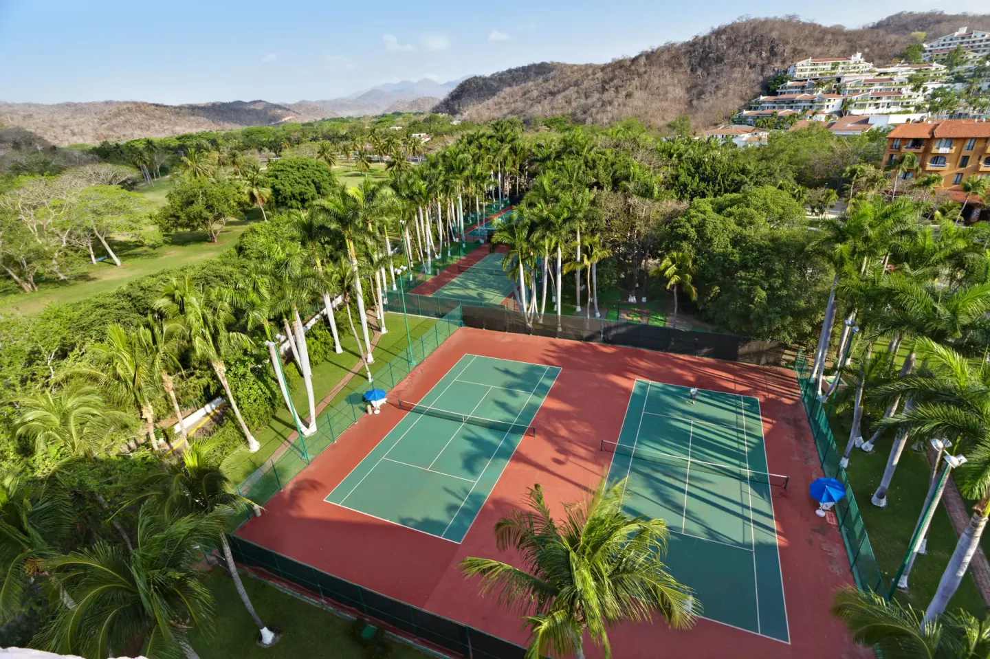 Tennis courts surrounded by palms and hills at Barceló Huatulco.