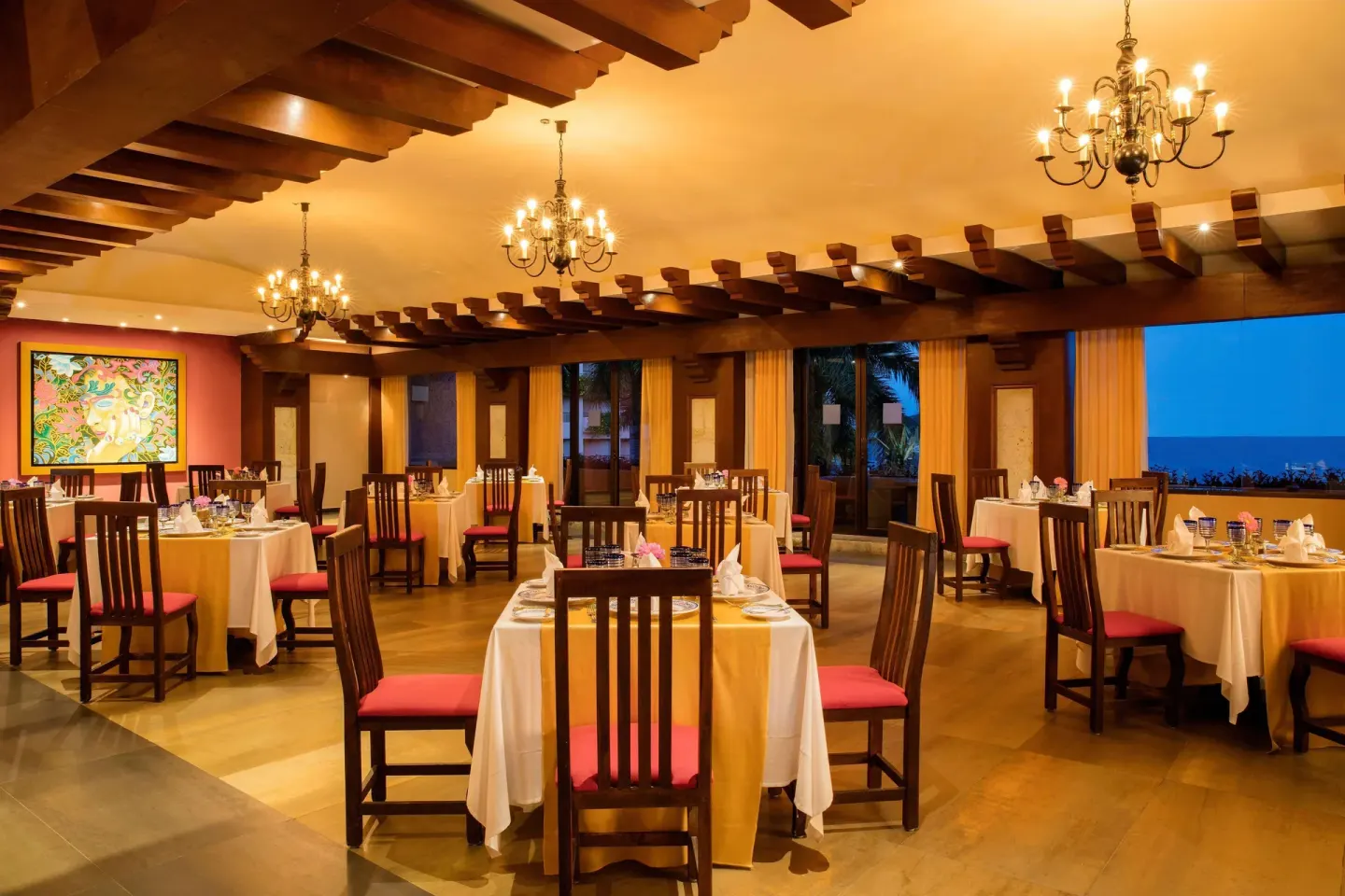 Warm restaurant dining room with chandeliers and sea-view windows at Barceló Huatulco.