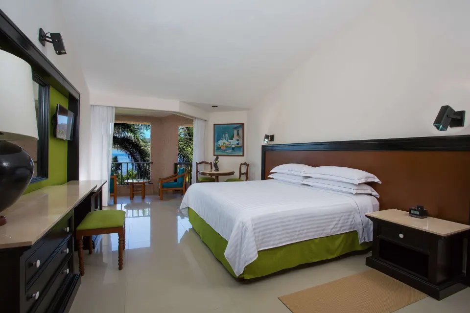 Deluxe Partial Ocean View king room with balcony and palm-framed water view at Barceló Huatulco.