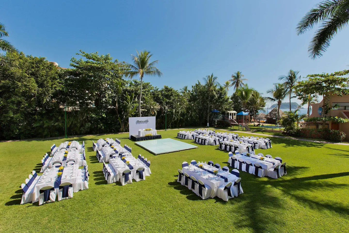 Outdoor lawn event with long banquet tables and a stage at Barceló Huatulco.
