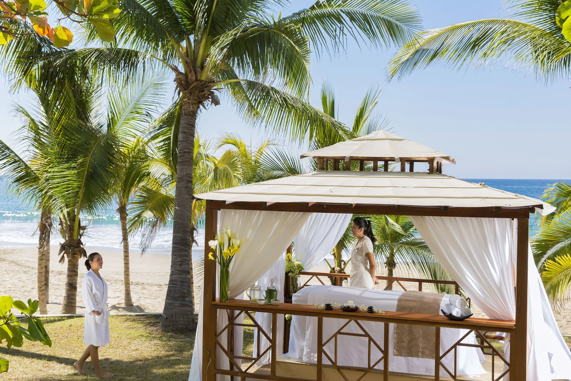 A beachside spa cabana with a massage table is set under palms at Barceló Ixtapa.