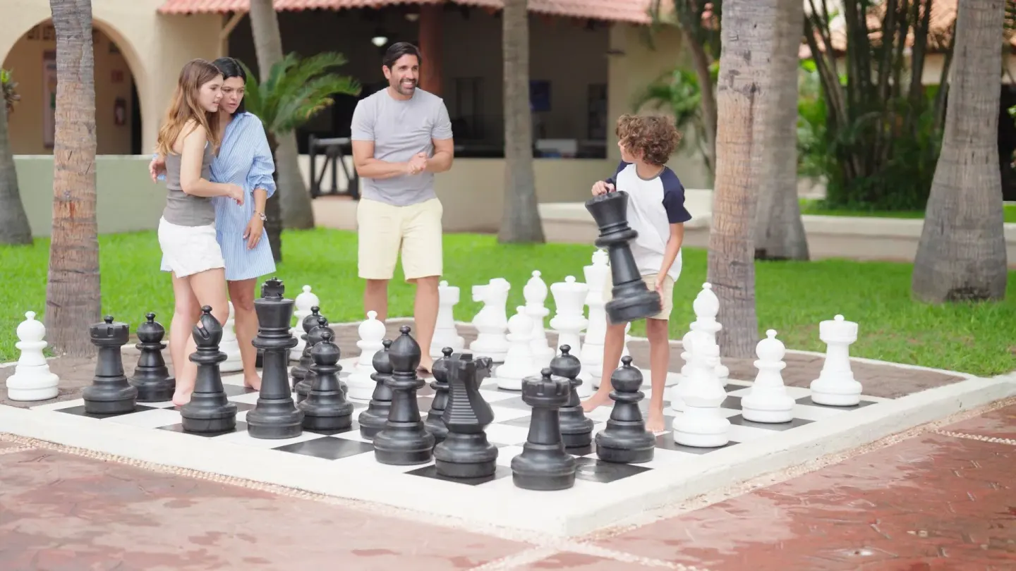 Family plays giant outdoor chess on a garden patio at Barceló Ixtapa.