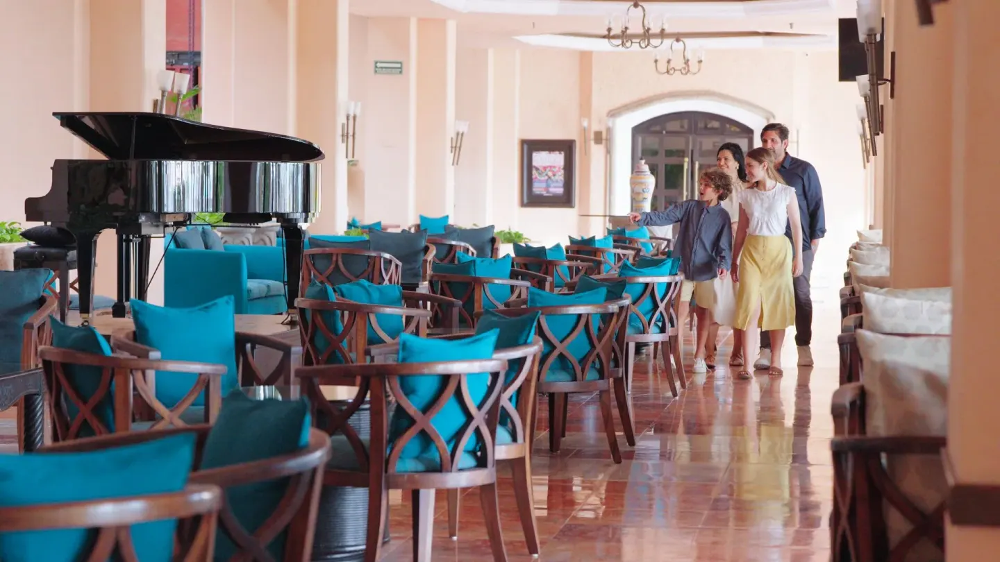 Lobby lounge with turquoise chairs, a grand piano, and walking guests at Barceló Ixtapa.