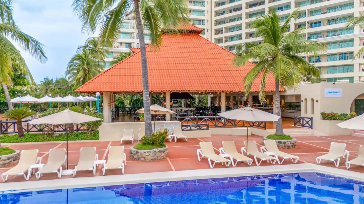 Pool deck with lounge chairs, palms, and Miramar restaurant at Barceló Ixtapa.