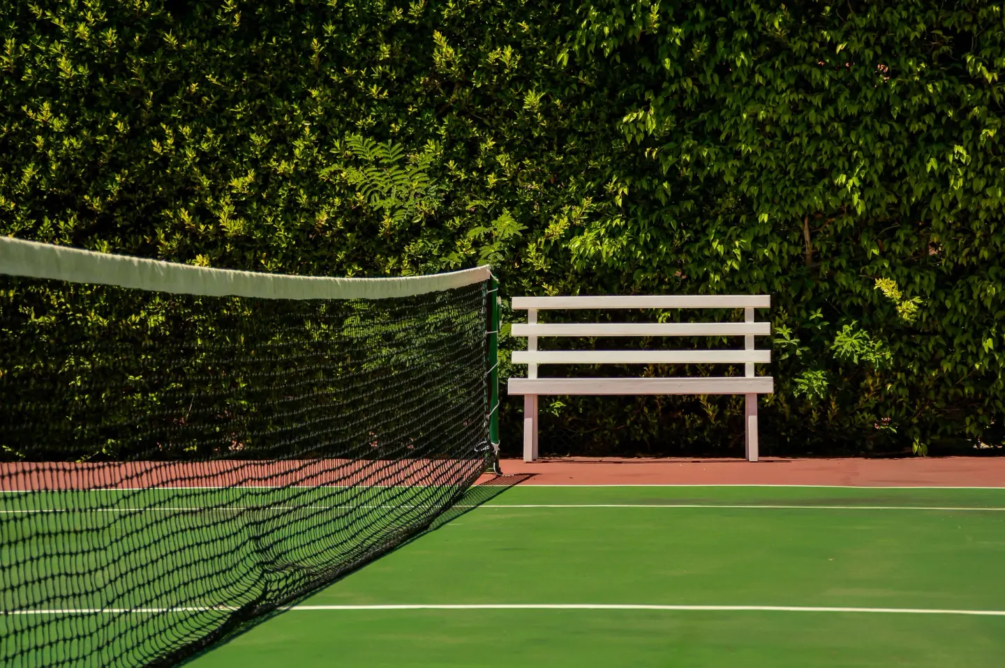 A tennis net and white bench sit beside a leafy hedge at Barceló Ixtapa.