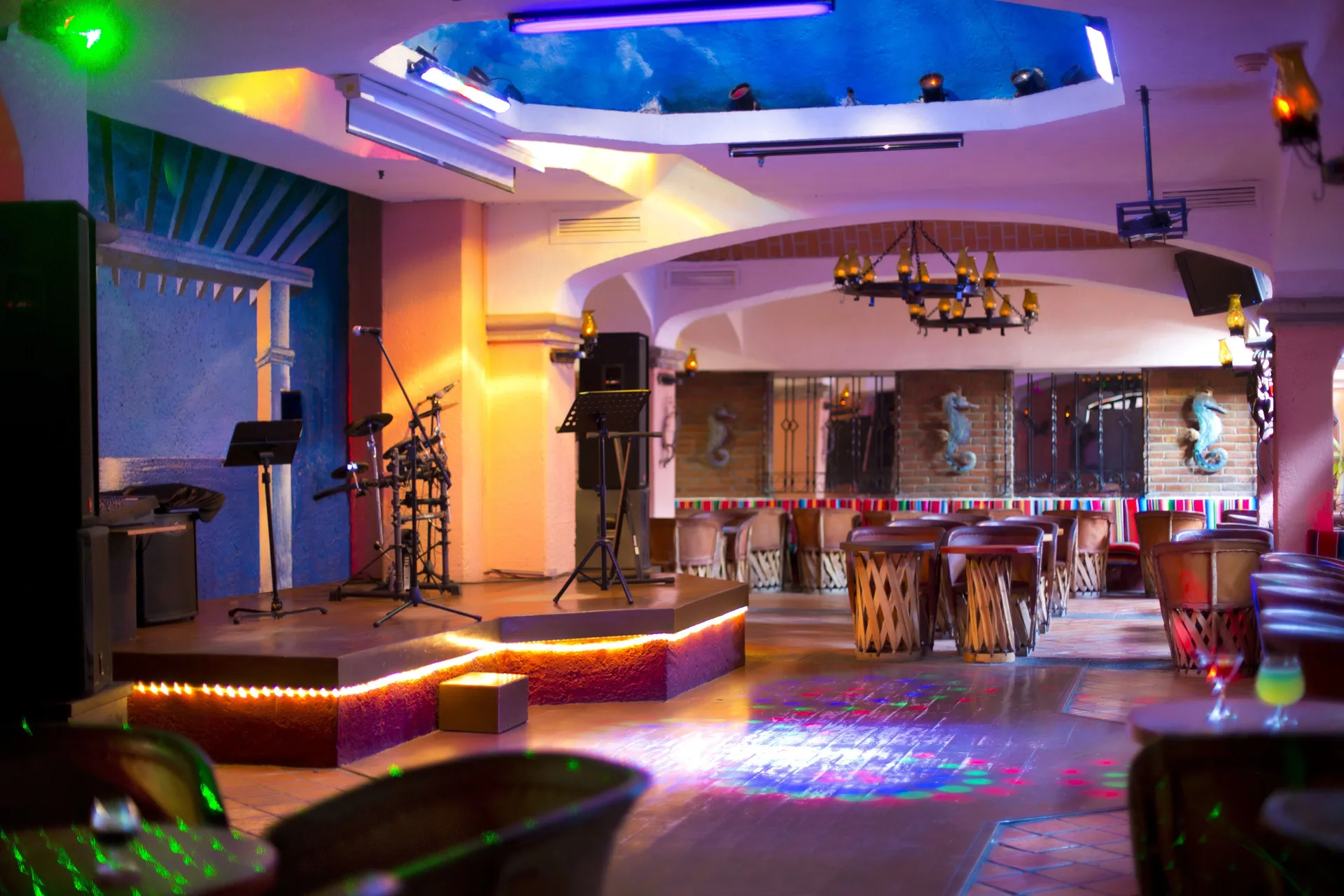 A bar lounge with a small stage, microphone, drum kit, and colorful lights at Barceló Ixtapa.