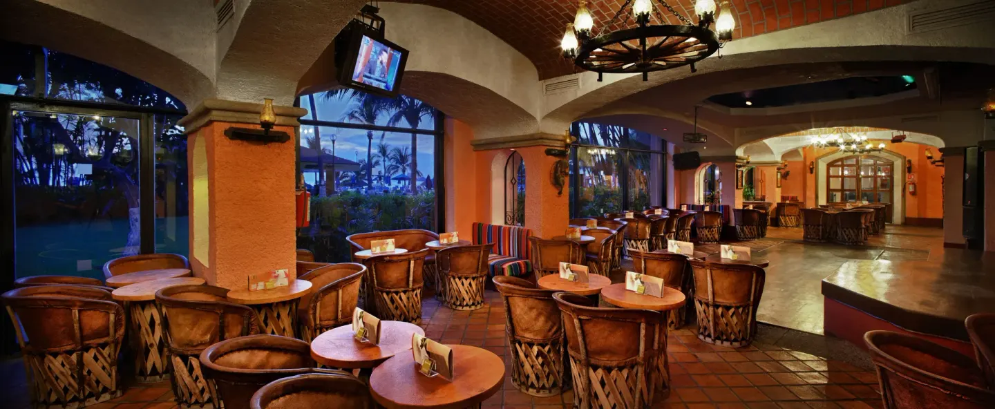 A lounge with round tables, woven chairs, arched ceilings, and large windows at Barceló Ixtapa.