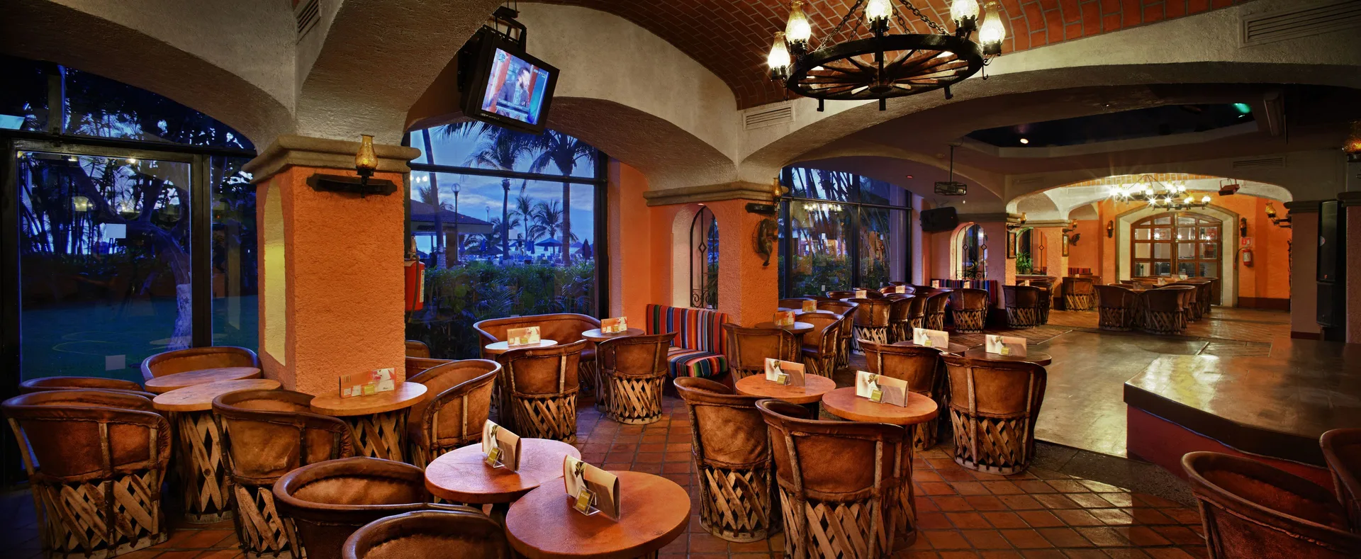 A lounge with round tables, woven chairs, arched ceilings, and large windows at Barceló Ixtapa.