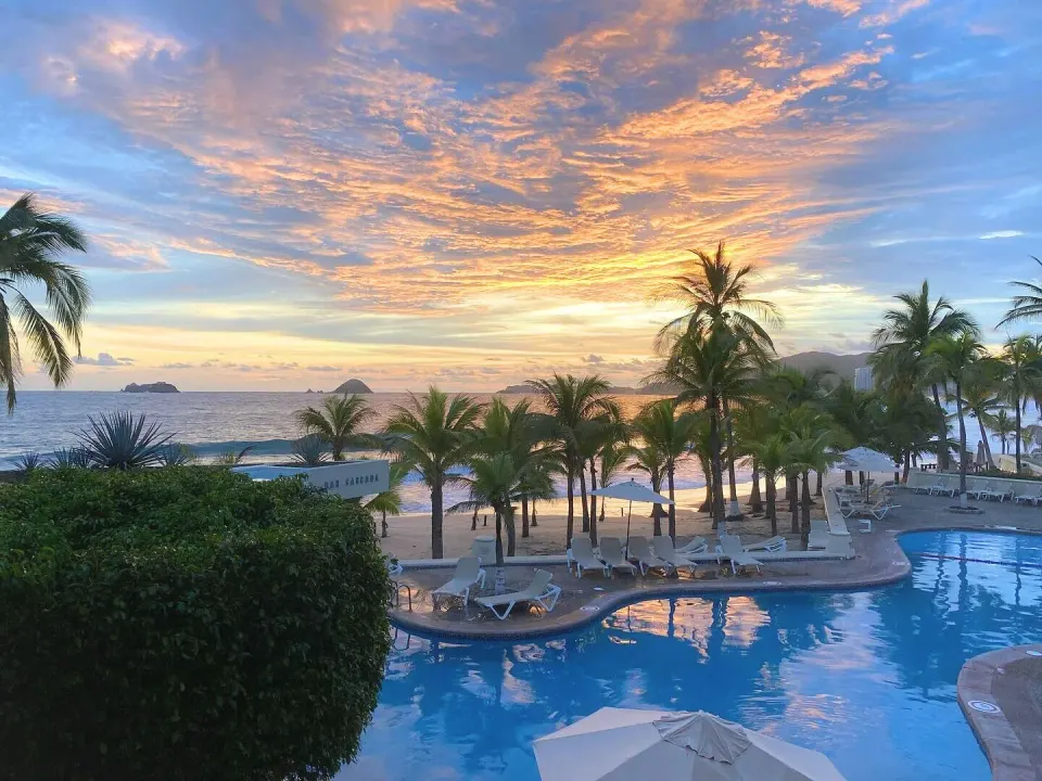 Family Villa pool and ocean sunset view at Barceló Ixtapa with palms and lounge chairs.