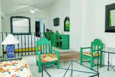 Family Villa sitting area with teal chairs, glass tables, and bedroom beyond at Barceló Ixtapa.