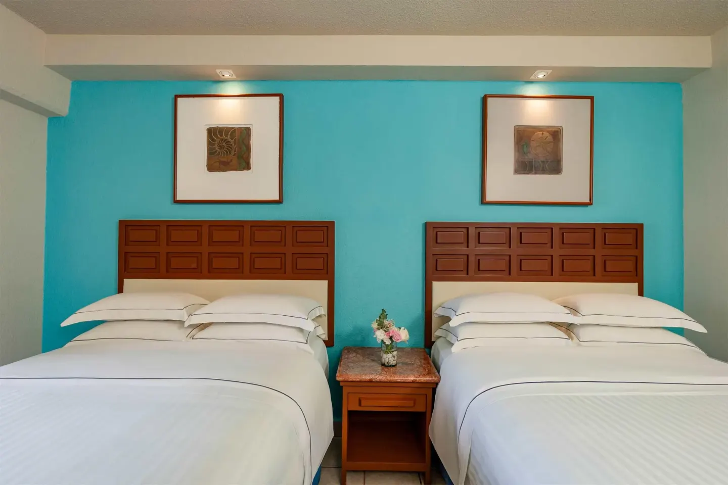 Superior Room Sea View with two beds, bedside table and turquoise wall at Barceló Ixtapa.
