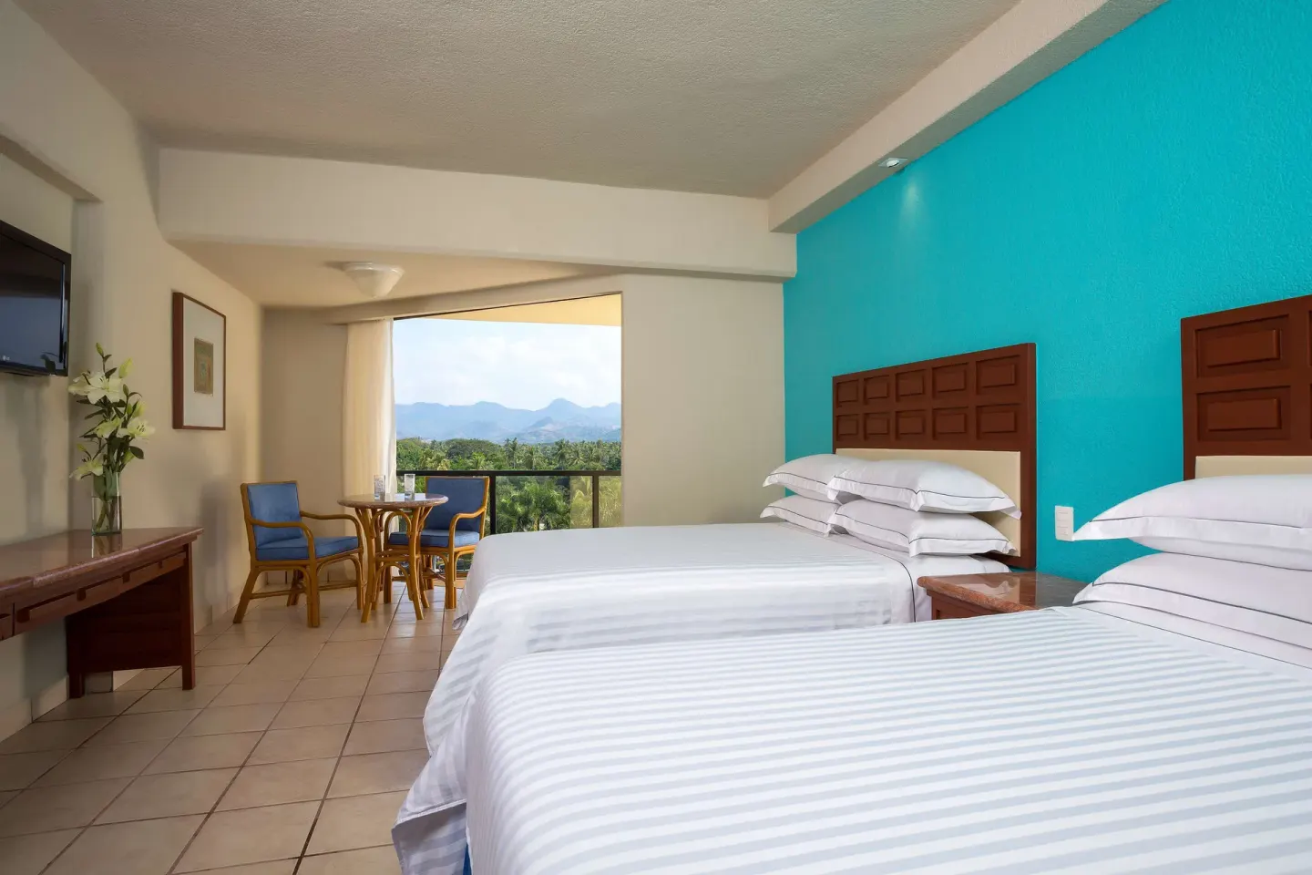 Superior Room with two beds, wall-mounted TV, and mountain-view balcony at Barceló Ixtapa.