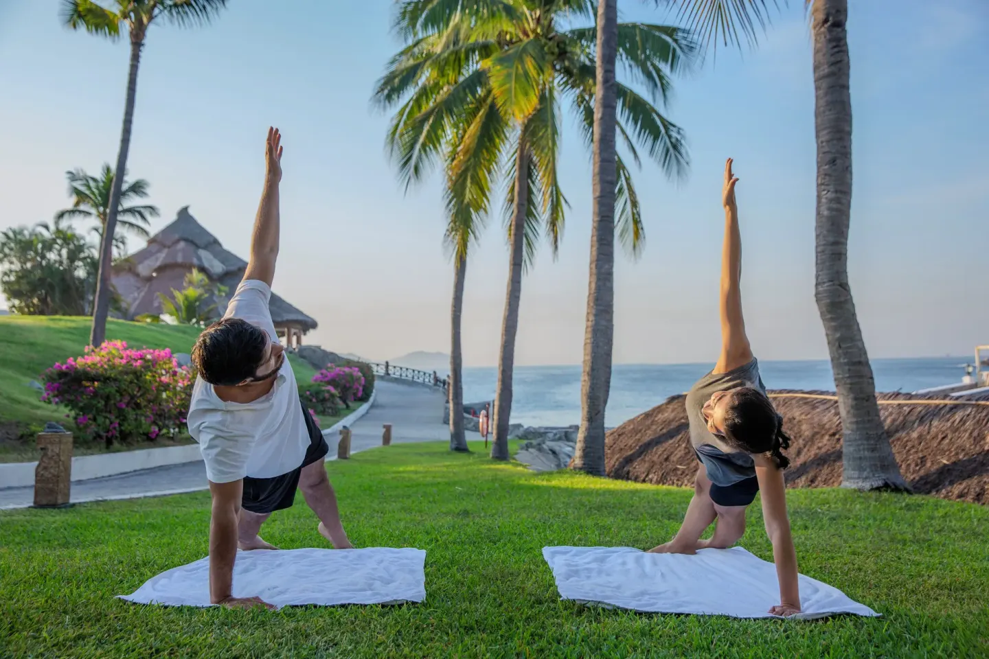 Two guests do yoga on a coastal lawn with palm trees at Barceló Karmina.