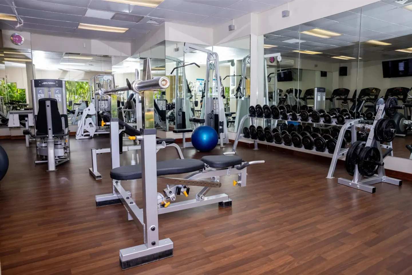 Fitness room with weight benches, dumbbells, mirrors, and cardio machines at Barceló Karmina.