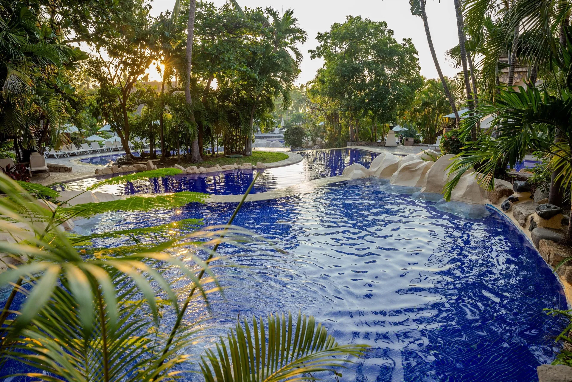 Curving blue pool surrounded by palms and greenery at Barceló Karmina.