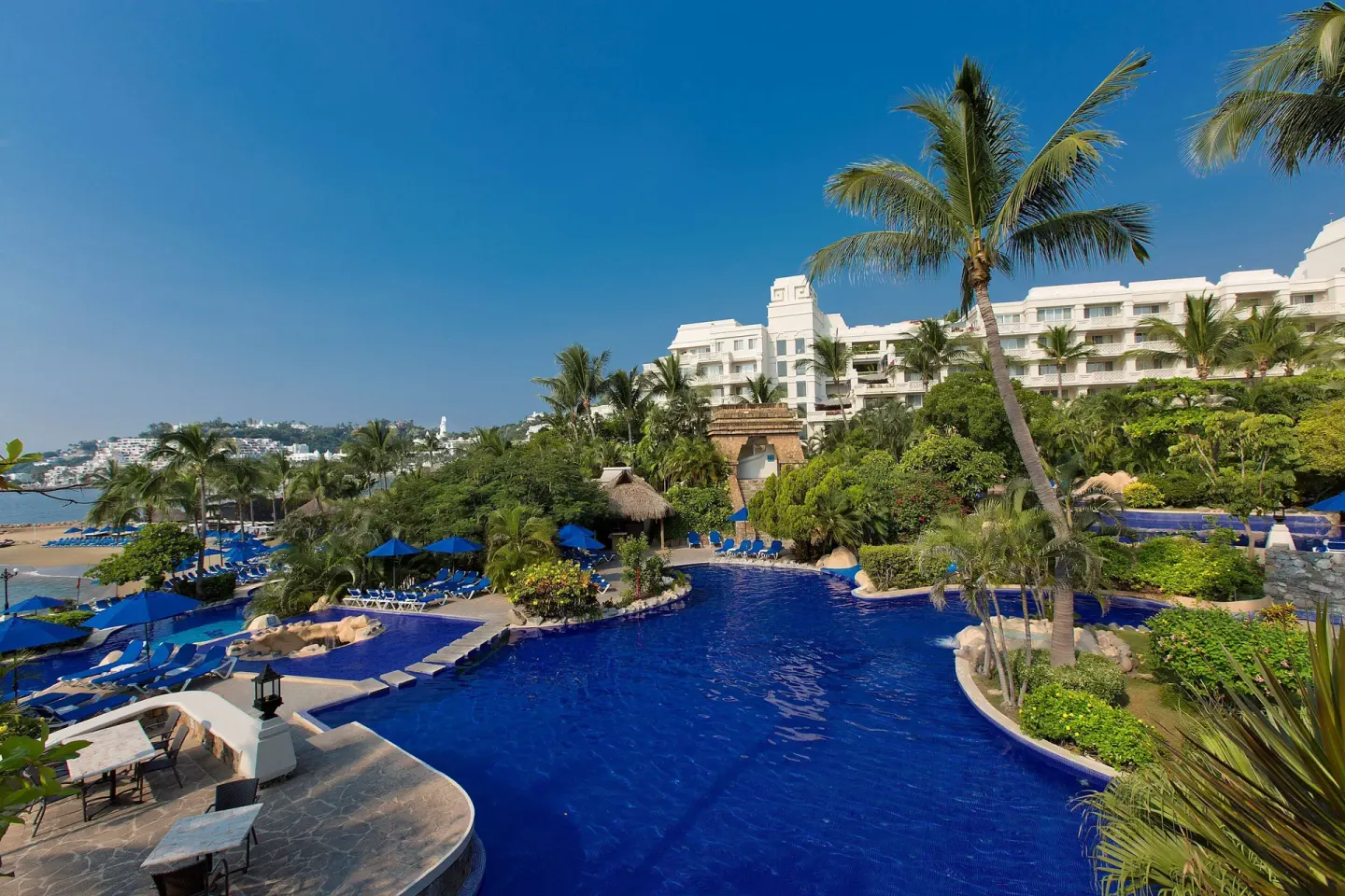 Resort pool, palms, beach umbrellas and white buildings at Barceló Karmina.
