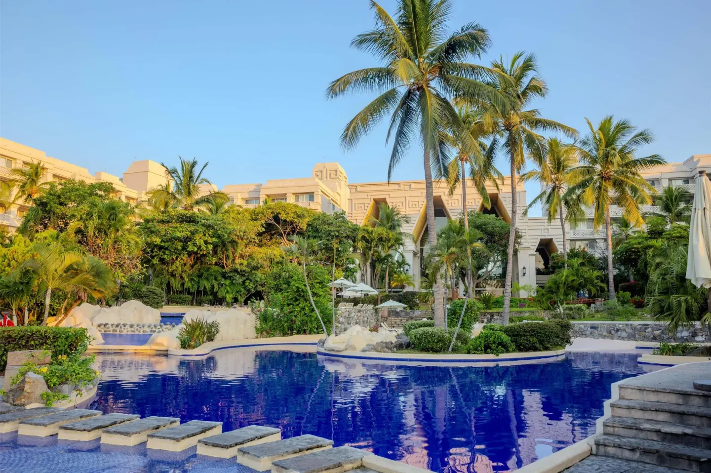 Palm-lined pool with stepping stones and resort buildings at Barceló Karmina.