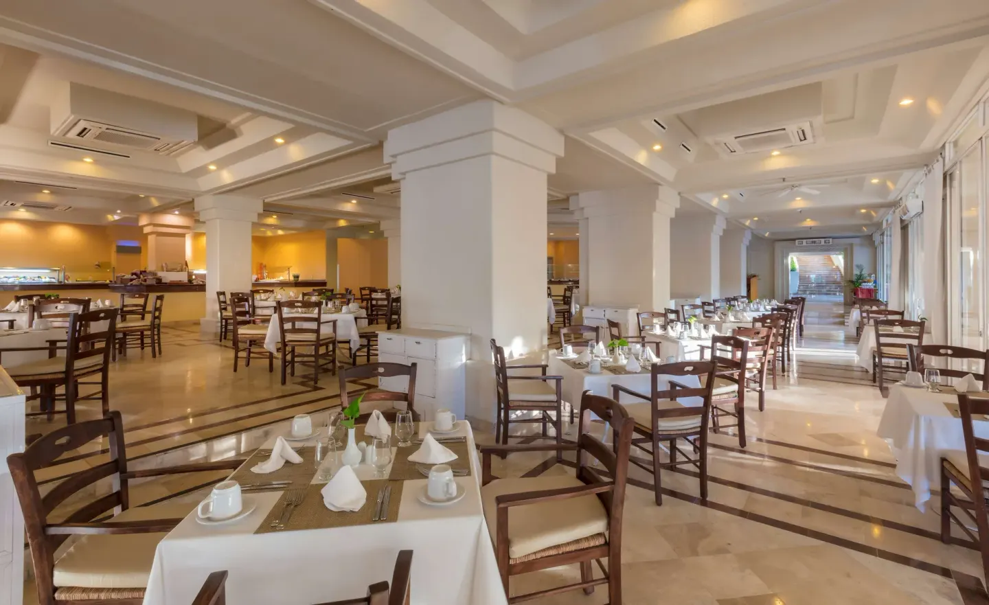 A bright buffet dining room with set tables and wooden chairs at Barceló Karmina.