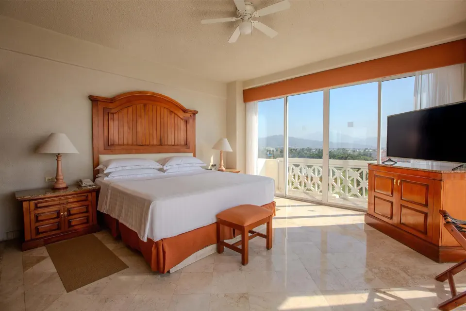 Master Suite bedroom with king bed, wood headboard, TV and balcony doors at Barceló Karmina.