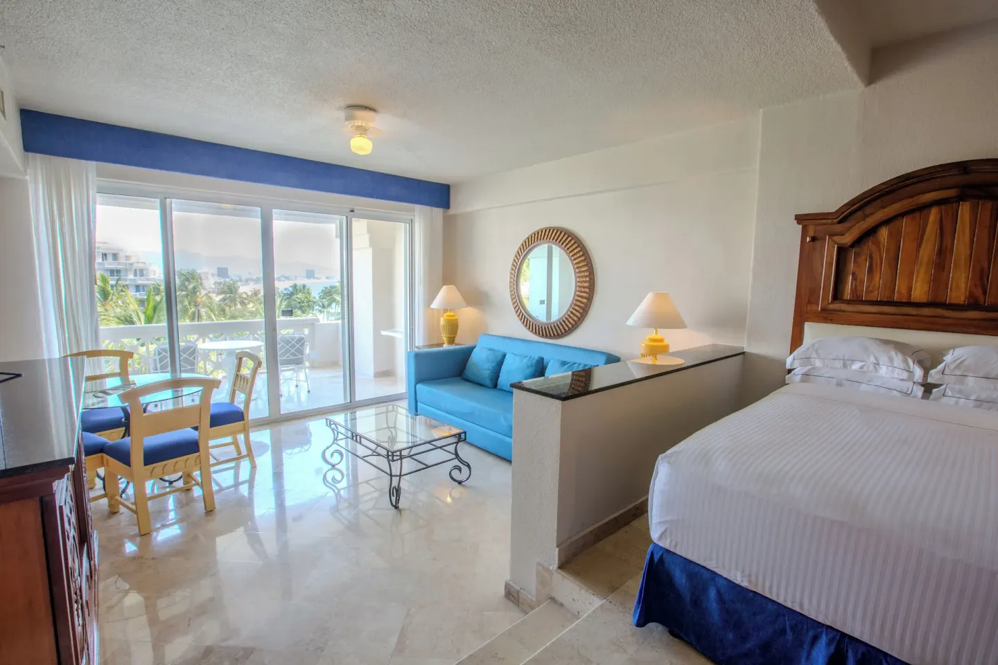 Suite Garden View with bed, blue sofa, dining table, and balcony at Barceló Karmina.