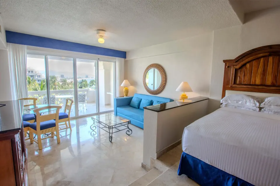 Suite Garden View room with bed, blue sofa, dining table, and balcony at Barceló Karmina.