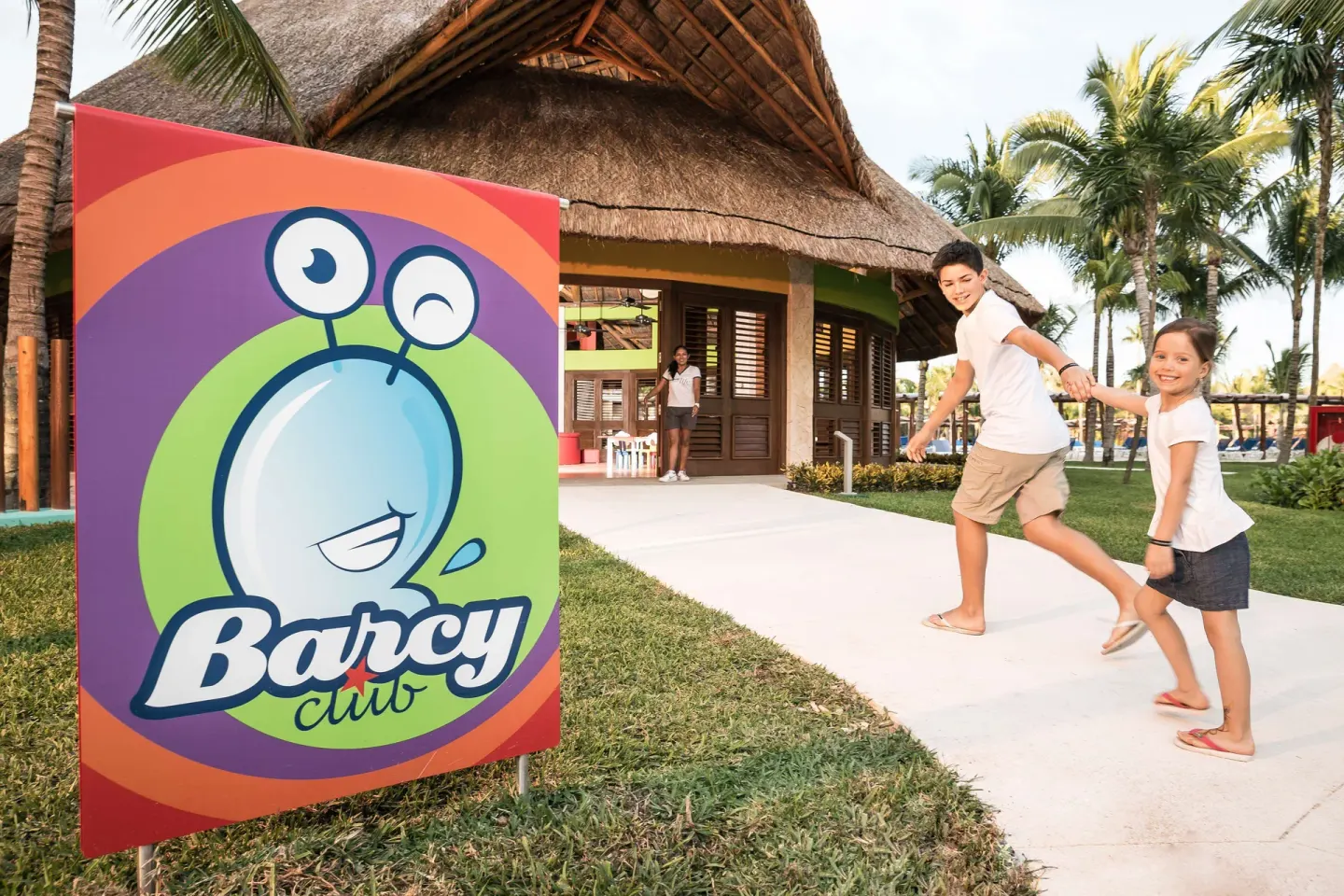 Children walking past the Barcy Club sign and thatched building at Barceló Maya Caribe.
