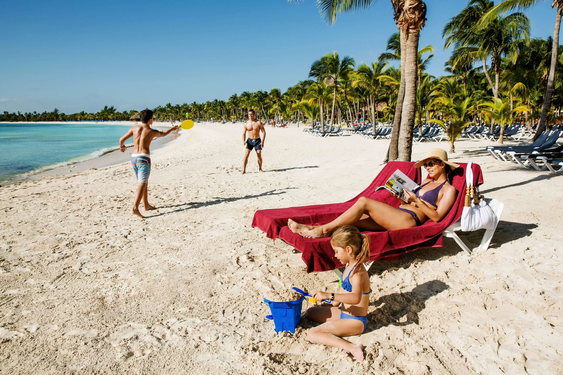 Guests relax and play on the beach with loungers and palms at Barceló Maya Caribe.