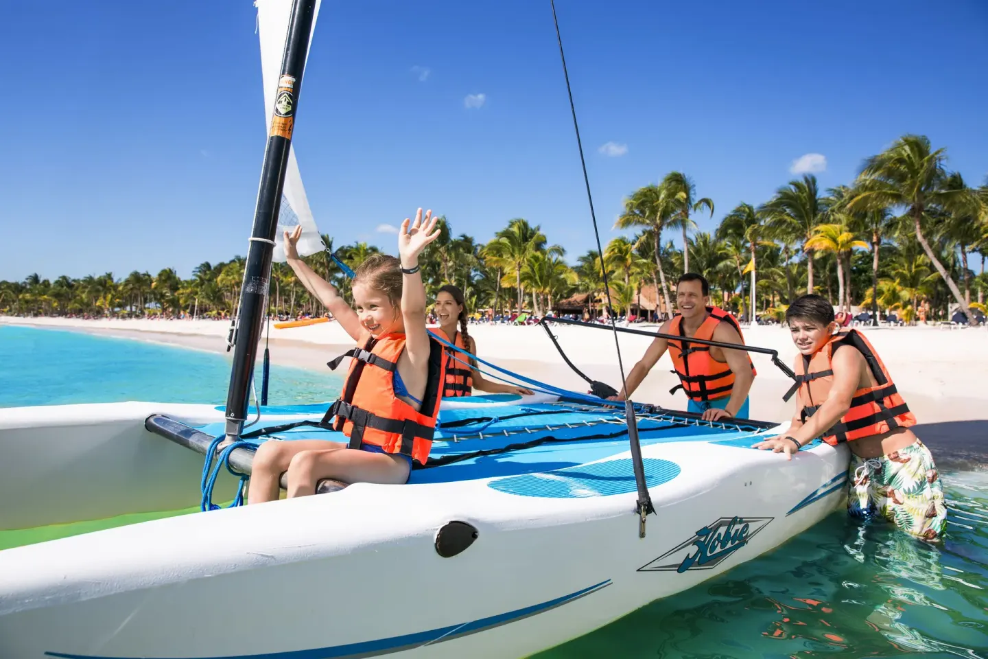 Family boarding a small sailboat in turquoise water at Barceló Maya Caribe.