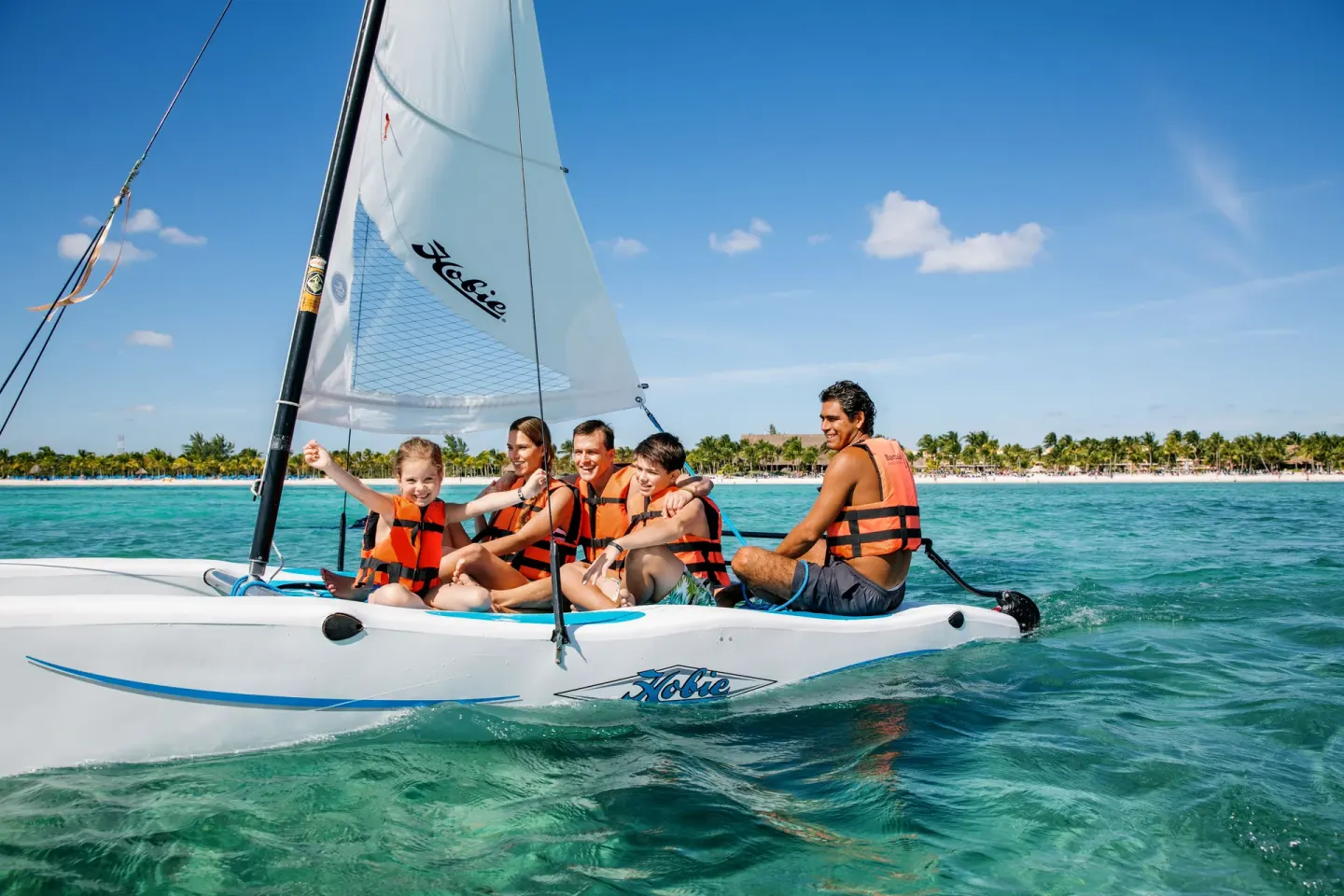 Family sailing a small catamaran on turquoise water at Barceló Maya Caribe.