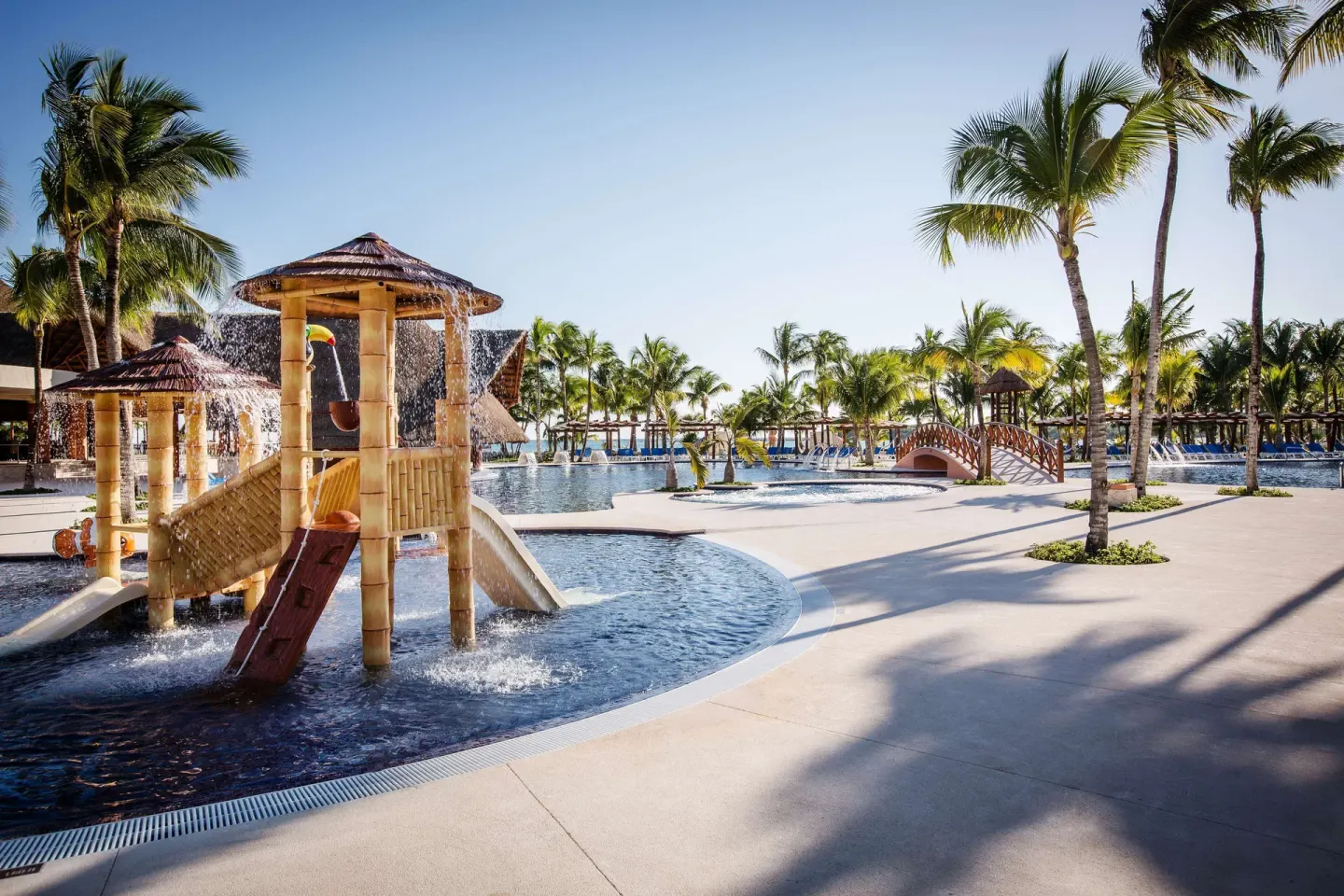 Children’s splash pool with slides, palms, and bridge at Barceló Maya Caribe.