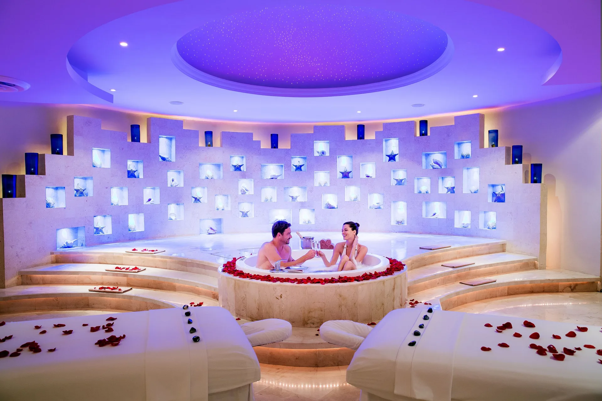 Couple soaking in a round spa tub with massage tables at Barceló Maya Caribe.