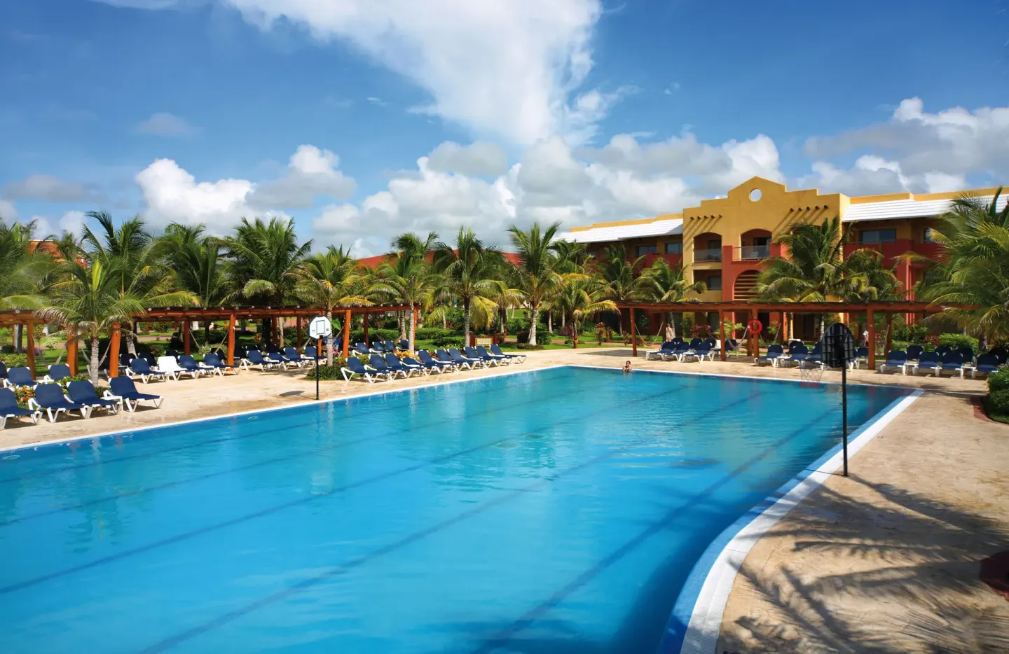 Large outdoor pool with loungers, palms, and guest buildings at Barceló Maya Caribe.