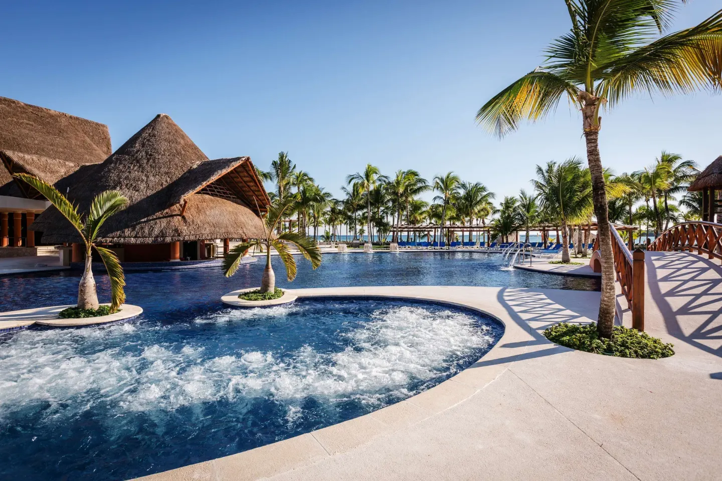 Pool with bubbling water, thatched roofs, palms, and bridge at Barceló Maya Caribe.