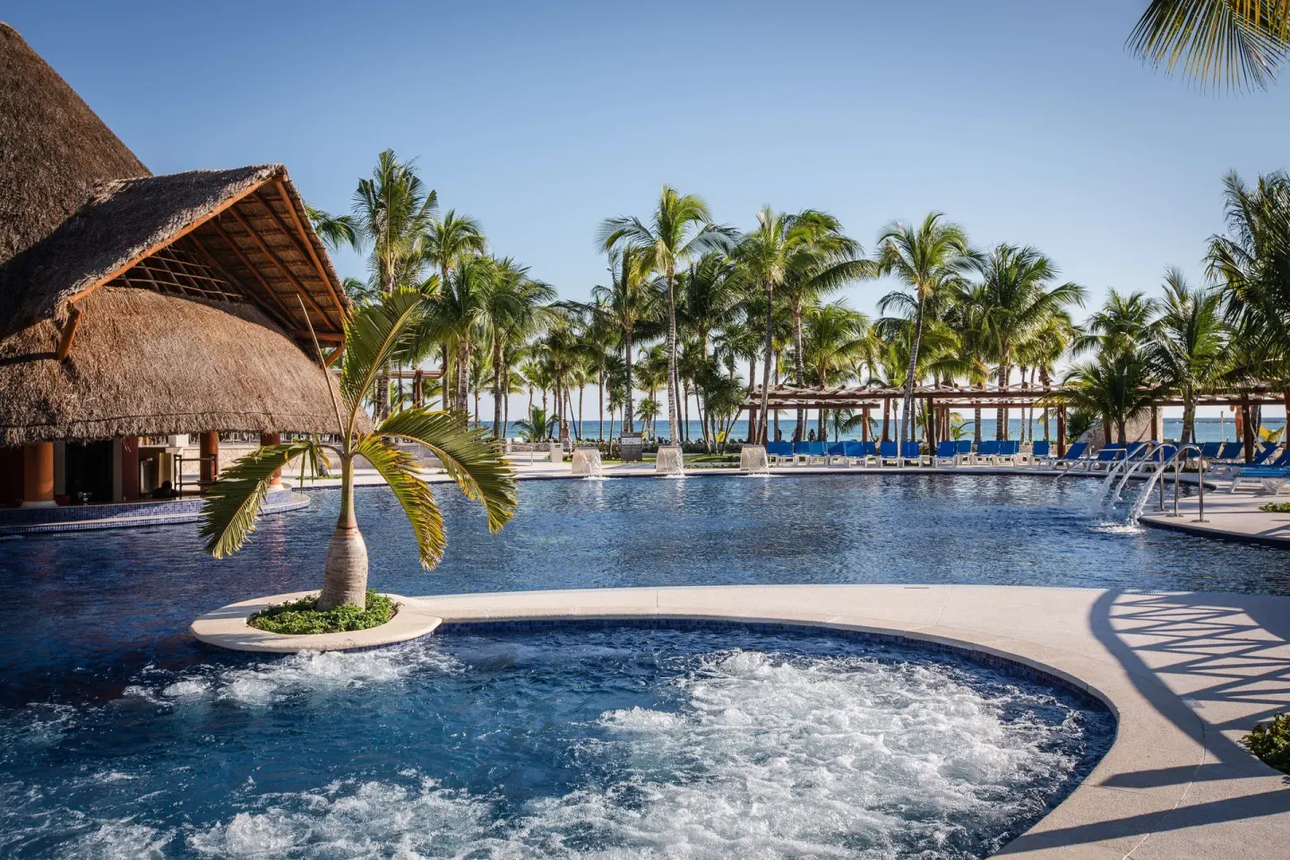 Pool and whirlpool area with palm trees and ocean beyond at Barceló Maya Caribe.