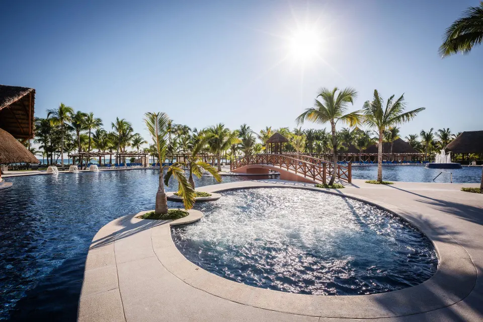 Sunny resort pool with palms, bridge, and whirlpool at Barceló Maya Caribe.