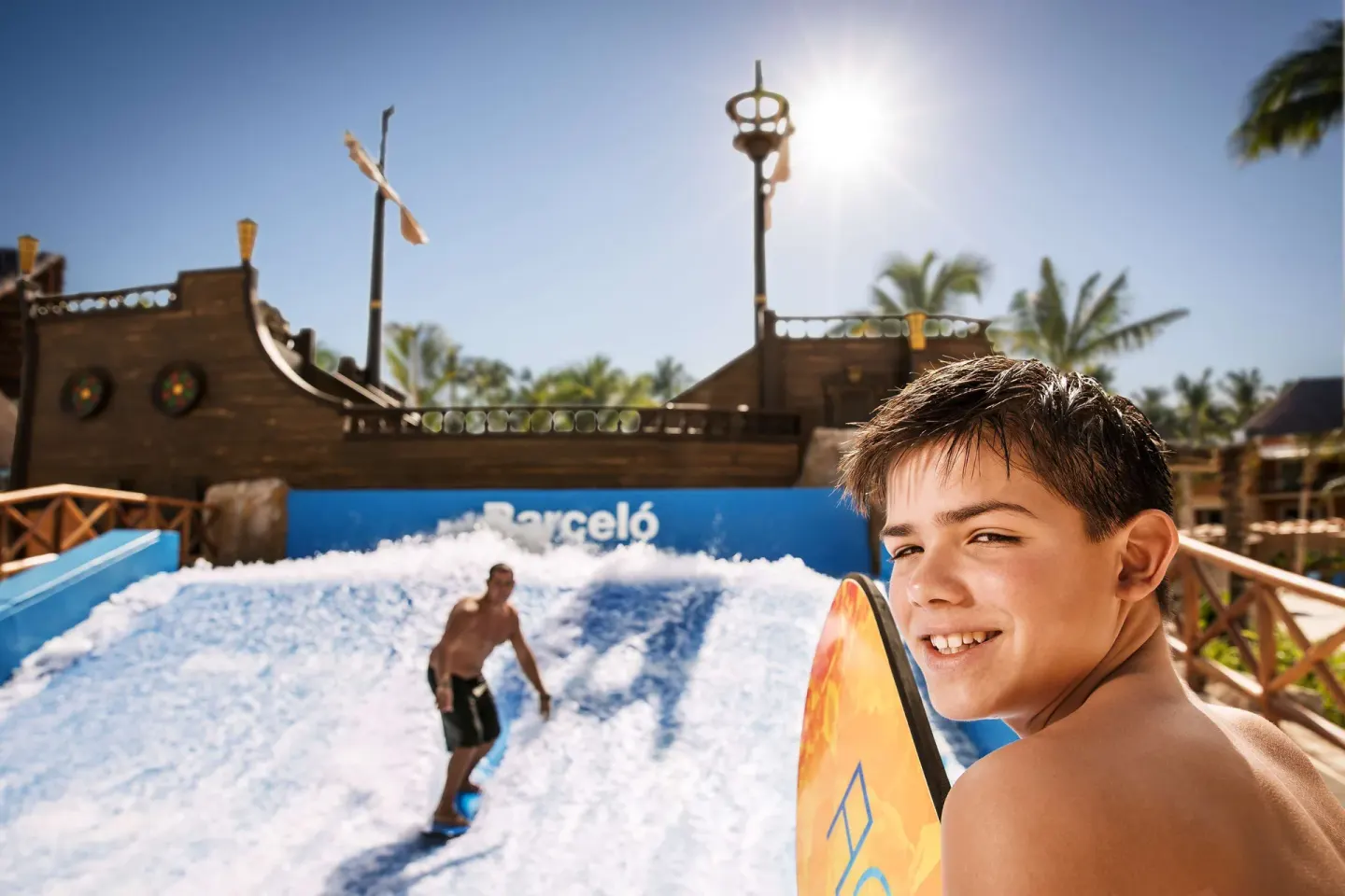 Boy holding a bodyboard beside the surf simulator at Barceló Maya Caribe.