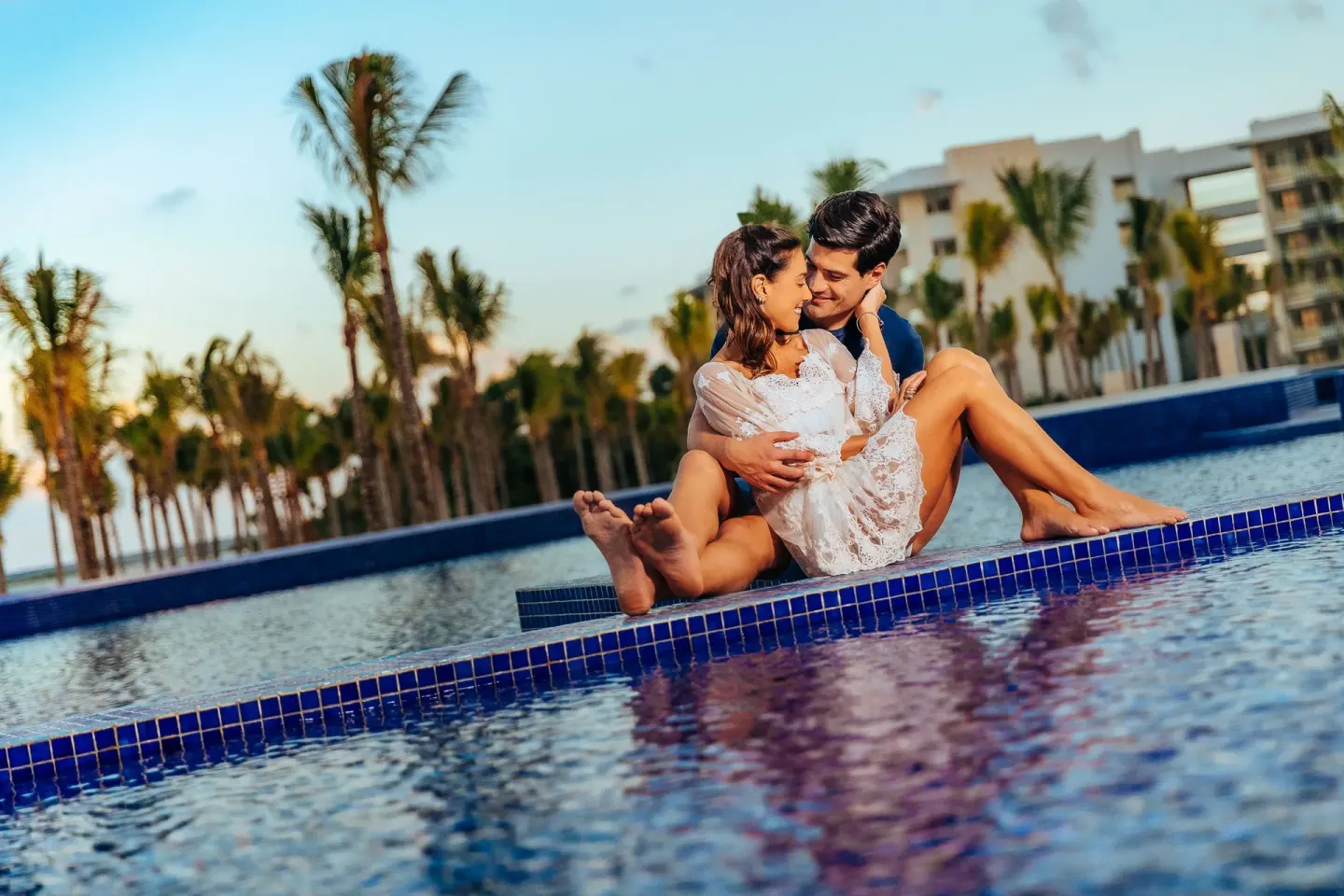 Couple sitting on the edge of a resort pool at Barceló Maya Riviera.