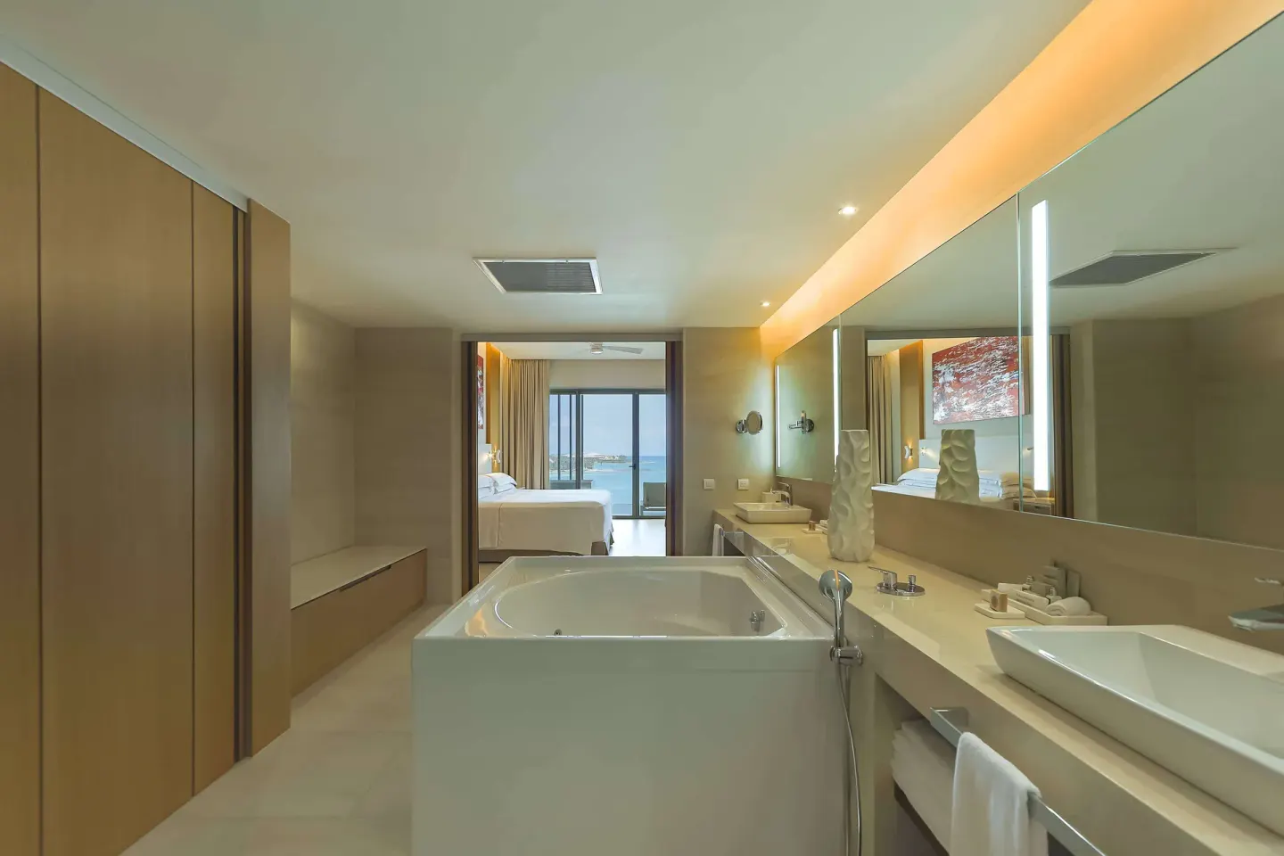 Guest bathroom with soaking tub, vanity, and bedroom beyond at Barceló Maya Riviera.